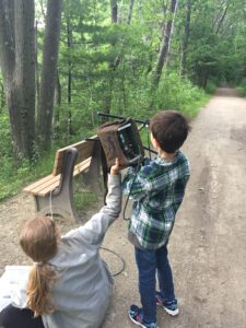 An elementary school student in a flannel shirt holds a radiotracking antenna at the side of a public path, and with help from a ZNE biologist, listens for the signal of a radiomarked turtle.