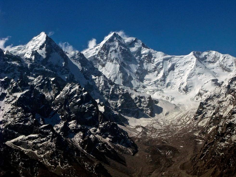 A photograph of tall, rugged, snow-covered mountains with clouds rolling off the highest peaks.